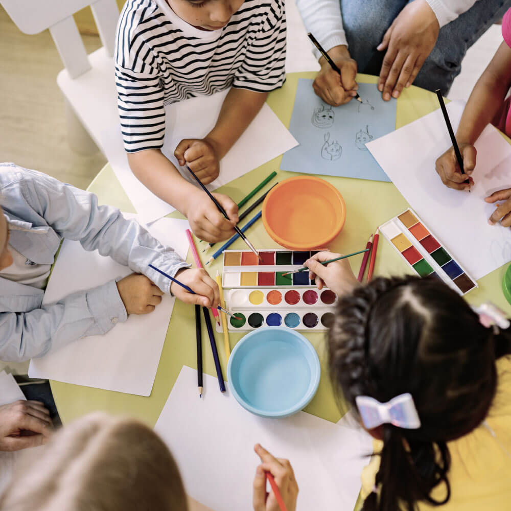 Barn som sitter på förskolan och målar tillsammans med en lärarvikarie